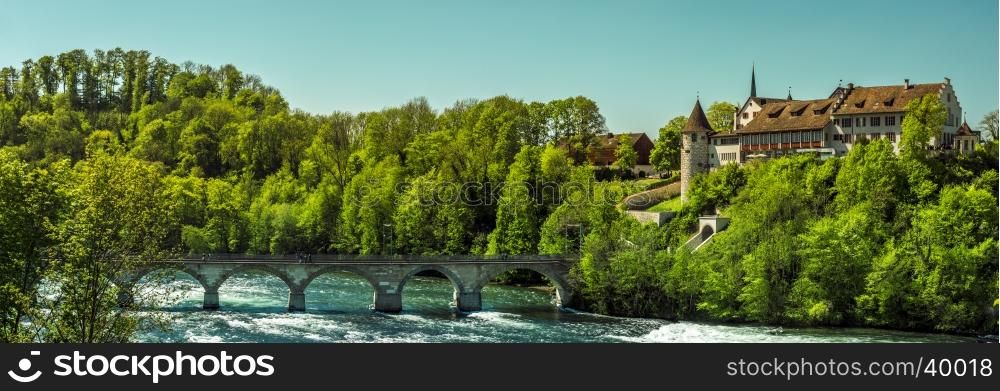 Panorama on a sunny day with the Laufen Castle surrounded by forest and a stone bridge over the river Rhine, in the Laufen-Uhwiesen town, Switzerland
