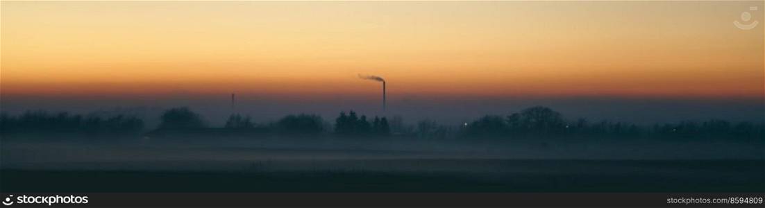 Panorama scenery with a smoking chimney in a misty sunset