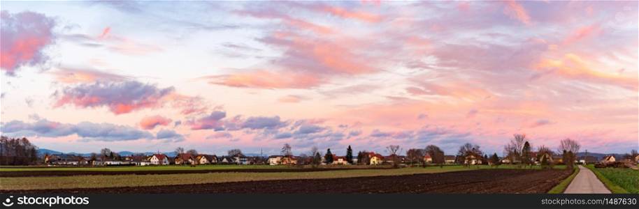 Panorama, sunset over fields and Austrian village with dramatic sky and colorful clouds. Sunset over village with dramatic sky, Panorama.