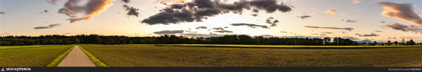 Panorama, sunset over fields in Austria with dramatic sunset sky and road leading to woods. Agriculture landscape.. Panorama, sunset over fields in Austria with dramatic sunset sky and road leading to woods.