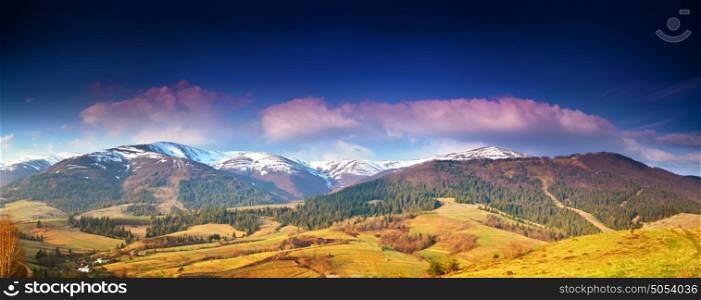 Panorama view of snow capped mountain peaks in spring time. Mountains in morning light. Deep blue sky. Idyllic Spring alpine morning landscape with fresh green meadows and snow-capped mountain tops in the background.