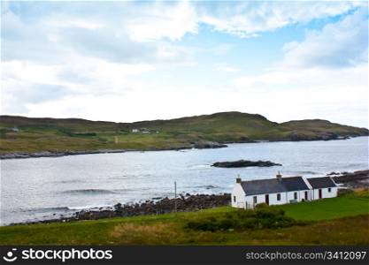 Panorama with a traditional Scottish house in front of a lake.