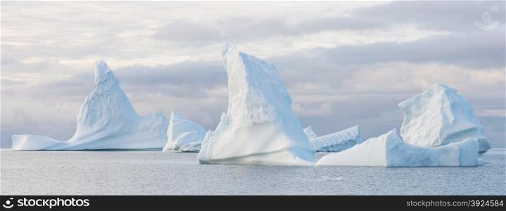 Panorama with beautiful icebergs. Panorama of beautiful icebergs in the sun and in front of a dark sky