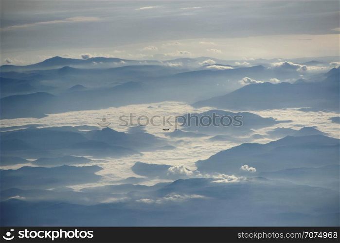 Panorama with flying plane high in sky above mountain ridge and clouds. Beautiful view from window of plane in evening. View from plane window. View from plane window to another plane flying over clouds and mountains
