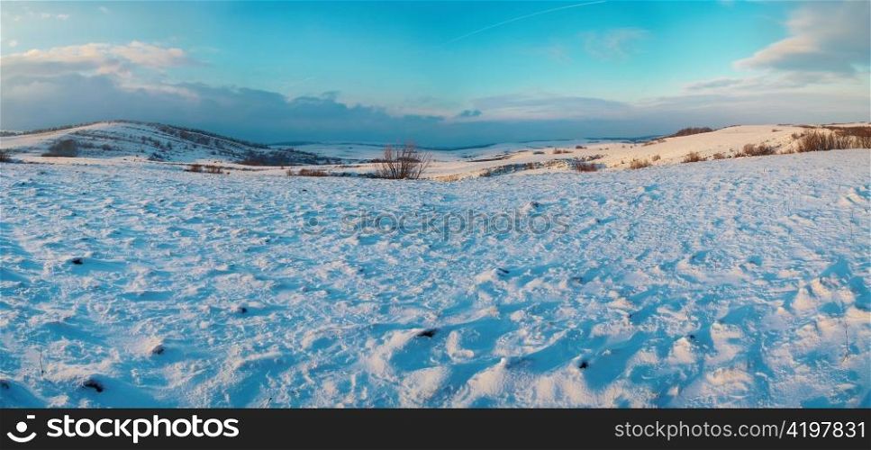 Panorama with winter hills covered by snow against sunset