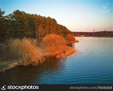 Panoramic landscape of lake shore with colorful trees in spring sunlight. April evening at the lake near Minsk, Belarus. Recreation zone aerial view. Beautiful sunset scene.