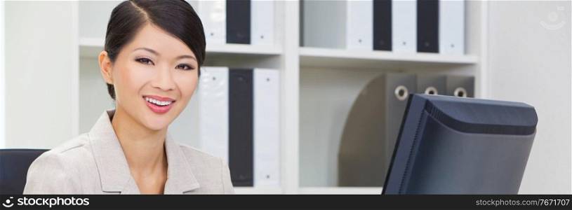 Panoramic portrait of a successful happy young Asian Chinese woman or business woman in office using a computer panorama web banner header