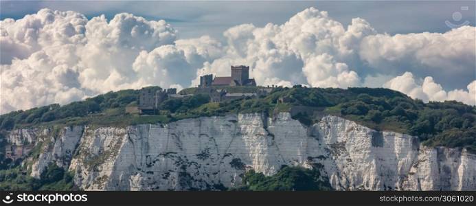 Panoramic shot of the White Cliffs of Dover and a castle on top of the cliff. Beautiful fluffy clouds in the background.