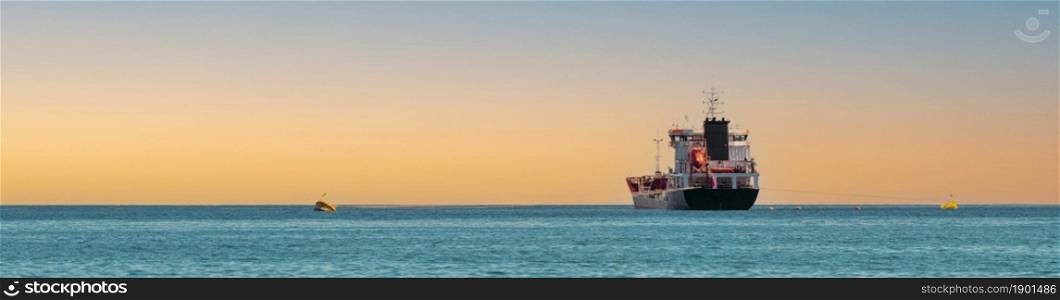 Panoramic shot of transport ship traveling on open sea at sunset.