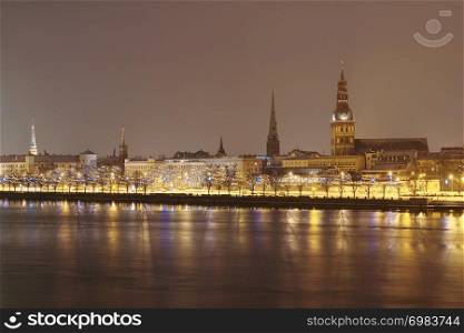 Panoramic skyline with 11th November Embankment illuminated for Christmas and New Year, Riga Castle, historic buildings, Churches and Cathedrals as seen over the frozen Daugava river in Riga, Latvia.