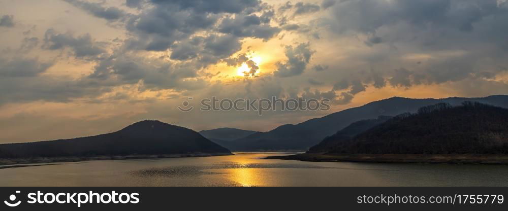 Panoramic view of a lake among hills and mountains with sun reflection