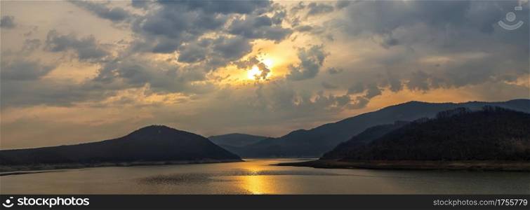 Panoramic view of a lake among hills and mountains with sun reflection