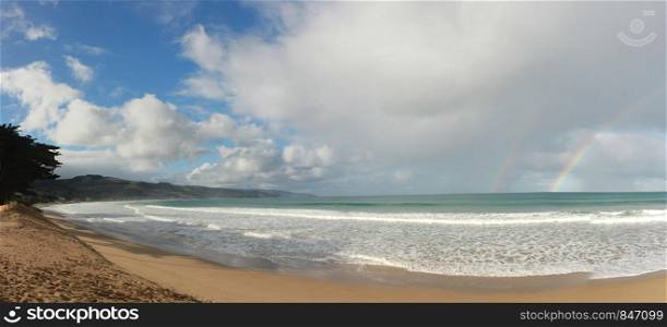panoramic view of a large clear rainbow stretching across the sky on a nice blue sky fluffy cloud day at Apollo Bay, coastal victoria, Australia