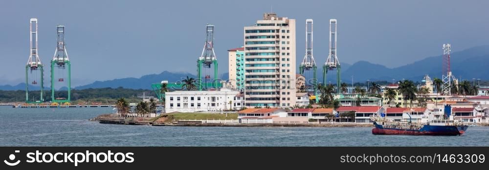 Panoramic view of a port in Panama next to Panama Canal. Massive shipyard cranes and buildings in the background, fuel tanker in the foreground.