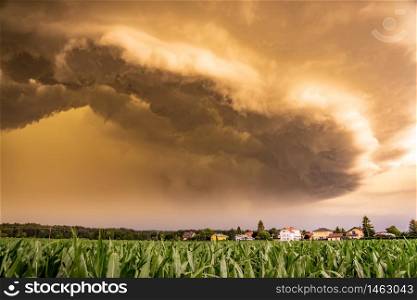 Panoramic view of a terrifying dark thunderstorm approaching small village. Flowing above corn fields.. Panoramic view of a terrifying dark thunderstorm approaching