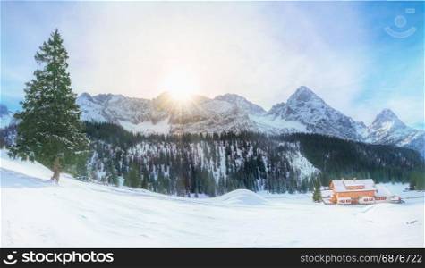 Panoramic view of an alpine village covered in snow and surrounded by the high peaks of the Alps mountains and their evergreen fir forests, located in Austria.