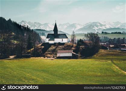 Panoramic view of beautiful mountain scenery in the Bavarian Alps with pilgrimage church of a hill and massif in the background, Bavaria, Germany