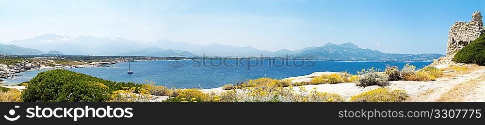 panoramic view of castle ruin in Corsica with mountains and sea in background
