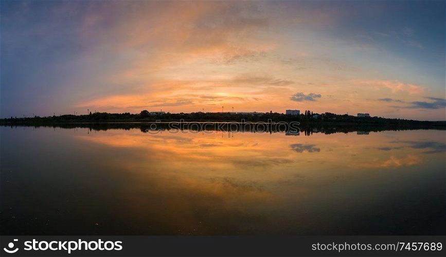 Panoramic view of colorful sunset clouds symmetric reflected on the lake surface. Idyllic summer evening, natural scene near a countryside pond with calm water.