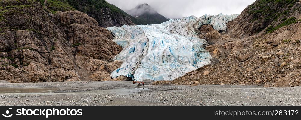 Panoramic view of Davidson Glacier in Alaska with tiny human figures approaching it in the distance