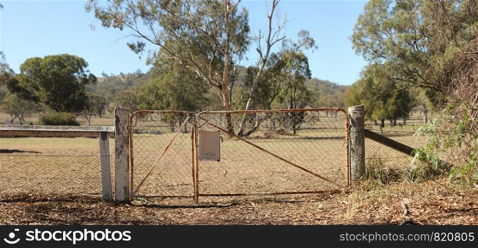 Panoramic view of old rusty deteriorating gates into a dry grassy field of native trees in rural New South Wales, Australia