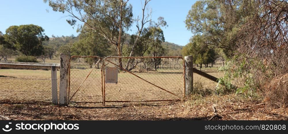 Panoramic view of old rusty deteriorating gates into a dry grassy field of native trees in rural New South Wales, Australia