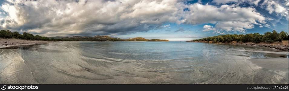 Panoramic view of Rondinara beach in Corsica with a calm mediterranean sea lapping onto the beach and dramatic sky above