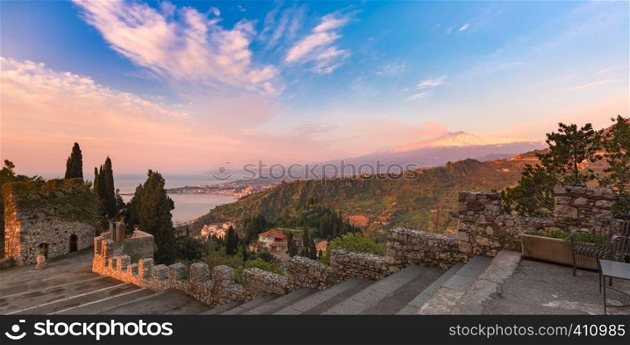 Panoramic view of smoking snow-capped Mount Etna volcano at sunrise, as seen from Taormina, Sicily. Mount Etna at sunrise, Sicily, Italy