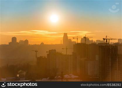 Panoramic view of sunset in the city with silhouette of buildings and industrial cranes. Sunset in the city