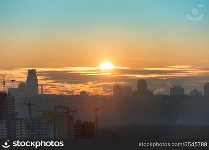 Panoramic view of sunset in the city with silhouette of buildings and industrial cranes. Sunset in the city