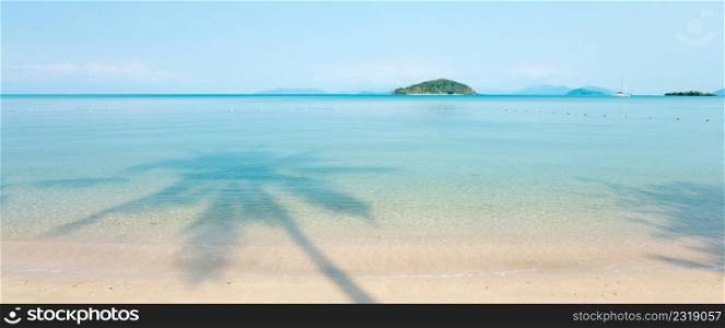 Panoramic view of tropical sea in summer, beautiful shadow of coconut palm tree on blue sea, yacht, green islands and light blue sky backgrounds. Sunshine day. Koh Mak Island, Trat, Thailand. Vacation time concept. Copy space.