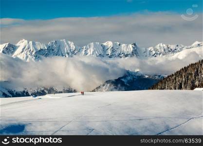 Panoramic View on Mountains and Two People Walking in French Alps in Winter