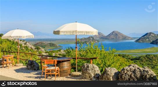 Panoramic view to Skadar lake and mountains from road cafe with tables, chairs and umbrellas, Montenegro