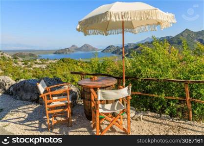 Panoramic view to Skadar lake and mountains from road cafe with tables, chairs and umbrellas, Montenegro