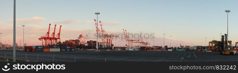 panoramic views of tall port shipping cranes standing tall loading a ship in port with shipping containers at Port Melbourne, with Melbourne city in the background, Victoria, Australia