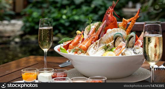 Panoramic web banner Bowl of groumet fresh seafood on ice with savory sauce serve with white wine glass on vintage wooden table. Restaurant gastronomy food and drink consumerism concept.