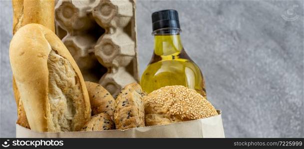 Panoramic web banner crop for Grocery bag with egg cooking oil and variety of bread in disposable paper bag on grey vintage loft background. Bakery food and drink and grocery concept for delivery.