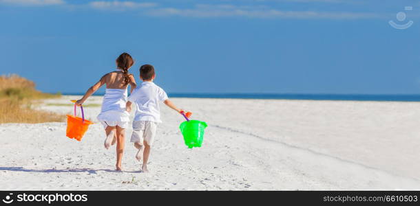 Panoramic web banner happy children, boy girl, brother and sister running and having fun playing in the sand on a beach with bucket and spade