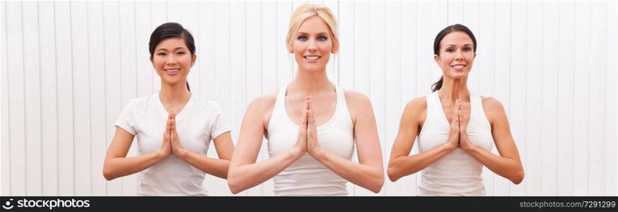 Panoramic web banner interracial group of three beautiful young women hands in prayer practising yoga at a gym or health club