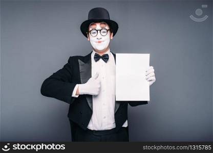 Pantomime actor performing with empty paper sheet. Comedy mime artist in suit, gloves, glasses, make-up mask and hat