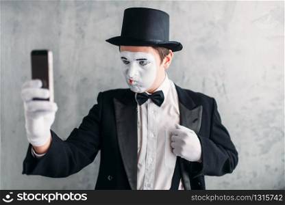 Pantomime actor with makeup mask makes selfie on camera. Comedy artist in suit, gloves and hat. Pantomime actor with makeup mask makes selfie