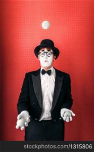 Pantomime male actor juggles with balls. Comedy mime artist in suit, gloves, glasses, make-up mask and hat. Circus juggler
