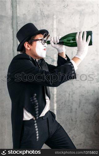 Pantomime theater actor performing with big bottle. Comedy mime artist in suit, gloves, glasses, make-up mask and hat