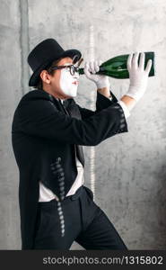 Pantomime theater actor performing with big bottle. Comedy mime artist in suit, gloves, glasses, make-up mask and hat