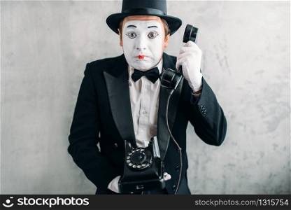 Pantomime theater actor with makeup mask performing with retro telephone. Comedy artist in suit, gloves and hat. Pantomime actor performing with retro telephone