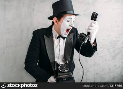 Pantomime theater actor with makeup mask performing with retro telephone. Comedy artist in suit, gloves and hat. Pantomime actor performing with retro telephone
