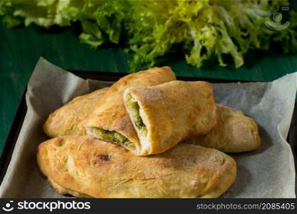 Panzerotti with escarole and grana padano baked in the oven with parchment paper. Close-up of panzerotti on green wood background and smooth and curly endive tufts in the background