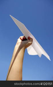 Paper airplane in children hand over blue sky