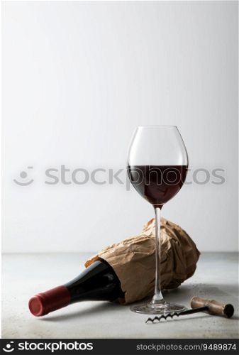 Paper bag with bottle of red wine and corkscrew with glass of wine on light board