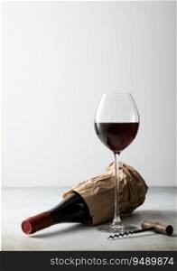 Paper bag with bottle of red wine and corkscrew with glass of wine on light board